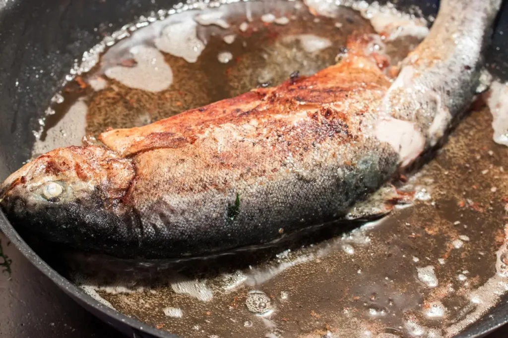 Melierte Forelle in der Pfanne am Braten mit viel Butterschmalz und Öl