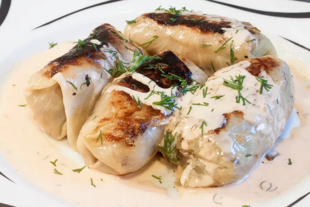 Kohlrouladen – klassisches Rezept wie bei Oma 13 Vier fertige Kohlrouladen liegen serviert auf einem weißen Teller in Soße und mit Dill garniert