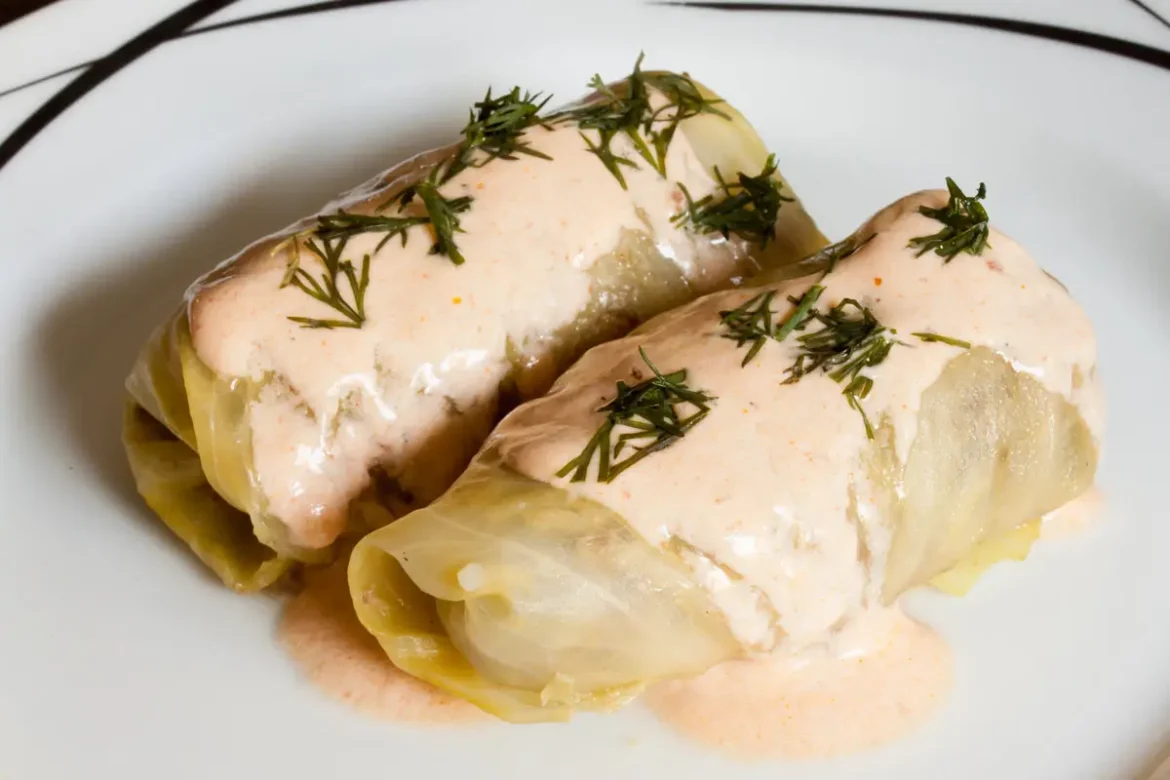 Zwei fertig gegarte und angebratene Kohlrouladen in Soße liegen auf einem weißen Teller